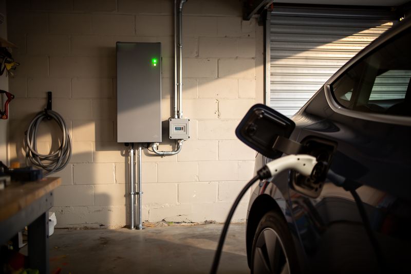 A home battery on a garage wall, with an electric car plugged in beside it