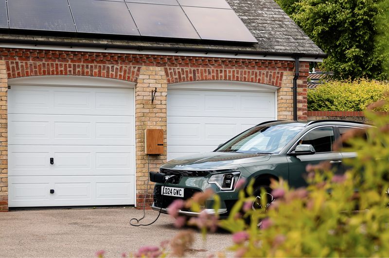 Electric car charging from a wall charger on a brick garage with solar panels on the roof
