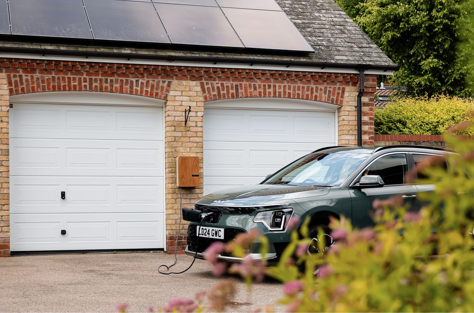 Elektrische auto aan een laadpaal bij een bakstenen garage met zonnepanelen op het dak